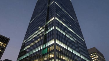 A sophisticated, low-angle photograph of a modern glass-and-steel skyscraper in a major North American tech hub at dusk. The building is illuminated with soft white and cyan lighting against a dark blue-gray night sky. The scene conveys technological power and corporate reliability.