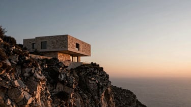 Wide panoramic shot of a dramatic Mediterranean coastline at sunset, a single modernist stone villa integrated into the cliff face, expansive sky, deep shadow tones