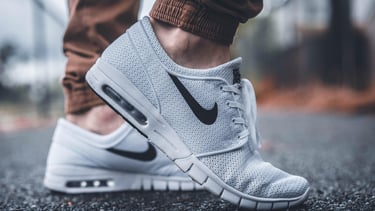 Close-up of a person wearing light gray Nike sneakers with mesh fabric on an urban street.