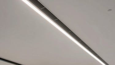 A crisp interior photograph of a modern commercial office lobby with high ceilings, showing a sleek linear diffuser air vent blowing fresh cooling air, professional architectural style.