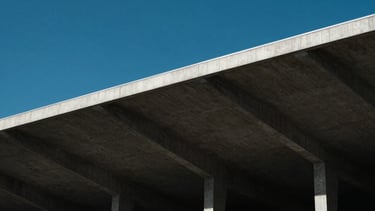 Architectural close-up of a modern concrete stadium roof against a crisp blue sky, dramatic natural light, high contrast, minimalist editorial sports photography.