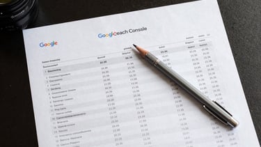 Overhead flat-lay of a printed Google Search Console report on a dark desk, rows of query data and impression numbers visible under neutral office light, a mechanical pencil resting across the sheet, tight crop emphasizing the data columns
