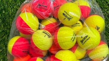 A clear bag of Srixon Z-Star Divide yellow and red dual-color golf balls on artificial green turf.
