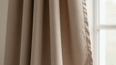 Close-up of premium warm taupe crepe fabric showing the delicate weave and clean stitching, warm editorial photography, soft natural window light, muted earth tones, elegant drapes, shallow depth of field, 35mm