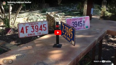 Weathervane-like object holding eight license plates all with numbers 3945 on them.