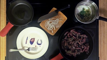 Sautéed beef in a cast iron skillet with sliced onions and a butter sauce on a black stovetop.