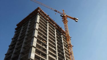 Low-angle heroic shot of a high-rise tower construction site with cranes, concrete structure, and architectural daylight.