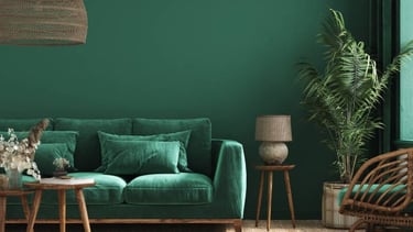 Sofá verde frente a una pared verde con mesa pequeña y flores empresa limpieza Marbella.