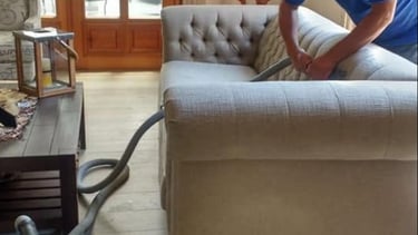 Professional upholstery cleaner deep cleaning a tufted beige sofa with a steam vacuum machine.