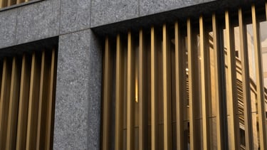 Detail of a modern building facade featuring graphite grey stone and golden metallic slats, reflecting a sophisticated South American design aesthetic.