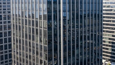 A high-angle professional architectural photograph of a futuristic glass skyscraper in a North American / US financial district. The scene is bathed in clean, bright daylight with deep navy and silver reflections on the glass. The composition is minimal and elegant, conveying a sense of world-class sophistication and technological leadership.