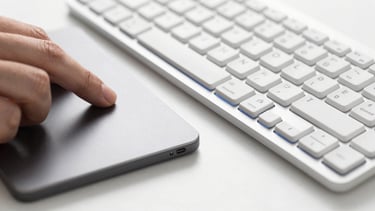Macro close-up of a designer's hand on a trackpad next to a clean mechanical keyboard, bright high-key studio lighting, sharp focus.