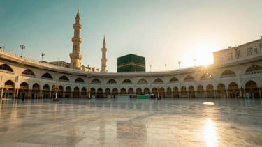 Wide panoramic environmental shot of the serene courtyard of the Grand Mosque in Makkah during dawn, soft golden-hour natural light casting long shadows, deep emerald and gold tones, 35mm lens