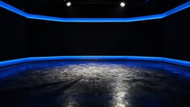 A wide, cinematic empty broadcast studio at night, dramatic blue rim lights reflecting off polished concrete floors, high-contrast shadows, 35mm