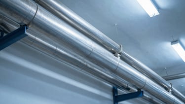 A clean stainless-steel air piping layout running along a bright factory ceiling, cool silver tones, high detail.