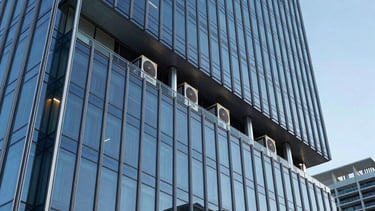 A high-end, futuristic office building in Miami at twilight with a sleek glass and silver steel facade. The lighting is deep blue and light cyan, highlighting the modern architecture. High-performance HVAC units are subtly integrated into the design, reflecting a sophisticated climate intelligence system.