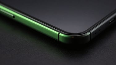 Macro studio photography of a sleek dark smartphone edge, low-key lighting, sharp neon green reflection on the glass boundary, deep charcoal background