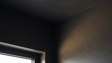 Extreme close-up of a perfectly sharp, clean interior corner where two Gyproc walls meet, painted in a deep charcoal color, with a subtle golden reflection from an unseen light source. High-contrast, geometric framing, architectural photography.