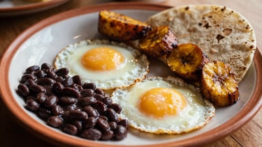 Traditional Latin breakfast plate with perfectly fried eggs, black beans, sweet plantains, and warm tortillas, morning daylight.