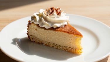 A slice of rich Tres Leches cake topped with fresh whipped cream and a hint of cinnamon, elegant dessert plate.