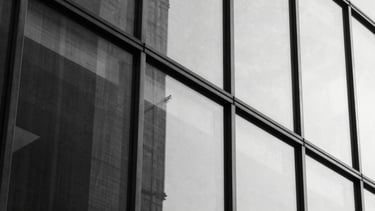 Abstract close-up of a glass facade reflecting sharp architectural lines, hard direct sunlight, high contrast, 35mm.