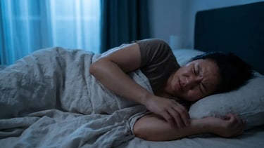 A sweating woman suffering from night sweats and sleep disturbance in a dark bedroom.