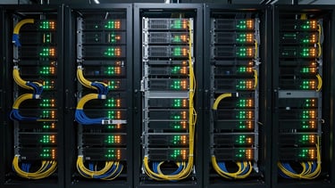 Overhead flat-lay of a dense server rack installation, cables organized in tight color-coded bundles, indicator LEDs glowing green and amber in a controlled technical environment, studio overhead lighting, no people, wide crop showing infrastructure scale