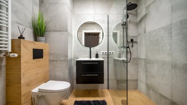 Nowoczesna łazienka z prysznicem walk-in, toaletą, umywalką i okrągłym lustrem.