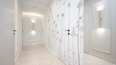 Jasny korytarz z jasną podłogą, drzwiami i ścianą z roślinną tapetą oraz kinkietami.