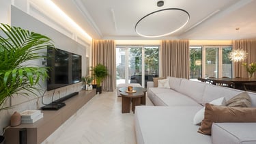 Nowoczesny salon z jasną sofą, stolikiem kawowym, telewizorem na ścianie i dużymi oknami