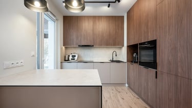 Nowoczesna kuchnia z drewnianą zabudową, wyspą kuchenną, piekarnikiem i zlewem.