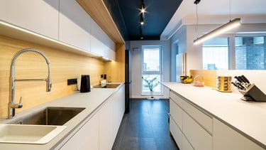 Nowoczesna kuchnia z białymi szafkami, drewnianym blatem i wyspą kuchenną.