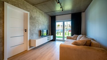 Salon z beżową sofą, szafką RTV z telewizorem, drzwiami i oknem tarasowym