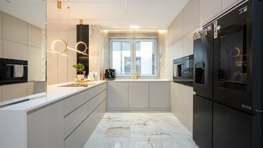 Nowoczesna jasna kuchnia z szarymi szafkami, białym blatem, czarną lodówką i oknem.