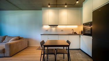 Nowoczesna kuchnia z białymi szafkami, czarną lodówką i stołem z czterema krzesłami