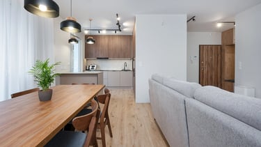 Nowoczesny salon z aneksem kuchennym, drewniany stół, sofa i wyspa kuchenna.