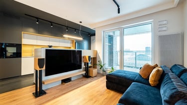 Nowoczesny salon z aneksem kuchennym, sofą, telewizorem i zestawem audio. Duże przeszklenia