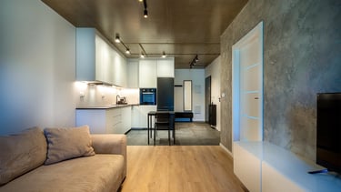 Nowoczesny salon z aneksem kuchennym, jasne meble, betonowy sufit i ściana TV.