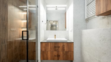 Nowoczesna łazienka z umywalką na szafce, lustrem, kabiną prysznicową i grzejnikiem.