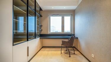 Nowoczesne, wąskie pomieszczenie z biurkiem pod oknem, krzesłem na kółkach i przeszklonymi szafkami 