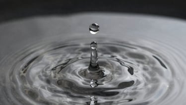 Macro shot of a drop of water falling into a still pond, creating perfect concentric circles. Black and silver tones, serene and precise.