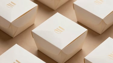 Clean minimalist branded takeout packaging boxes with elegant corporate logos, curated flat lay composition with warm earthy tone backgrounds, professional lighting.