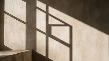 A close-up of natural sunlight casting sharp, architectural shadows on a warm, textured ivory stone wall, minimalist and calm