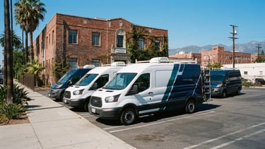 Sharp industrial photograph of liveried company service vehicles parked outside the Pasadena brick office under bright California sunlight, 35mm.