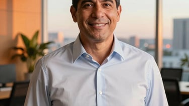 A professional portrait of a mentor in a modern office in Miami, Latinoamerica / EE.UU., wearing a crisp shirt, looking friendly and approachable at the camera, warm natural lighting from a large window, Sunset Orange accents in the background decor, professional photography style.