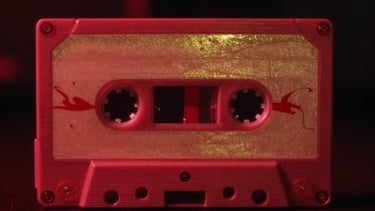 Atmospheric vintage cassette tape close-up, crimson neon glow, gold reflections, 35mm film grain, deep shadows