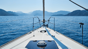 Desde la proa de un velero, paisaje de montañas al fondo y mar en calma