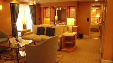 Vista da suíte luxuosa em navio de cruzeiro, com decoração refinada e amplo espaço interno.