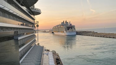 Navios de cruzeiro ancorados em porto italiano, com paisagem costeira ao fundo.