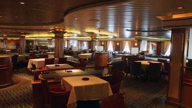 Restaurante elegante a bordo de navio de cruzeiro, com mesas arrumadas, iluminação suave.